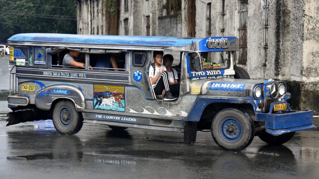 A colorful jeepney on a Philippine road, with passengers seated inside, illustrating public transport.