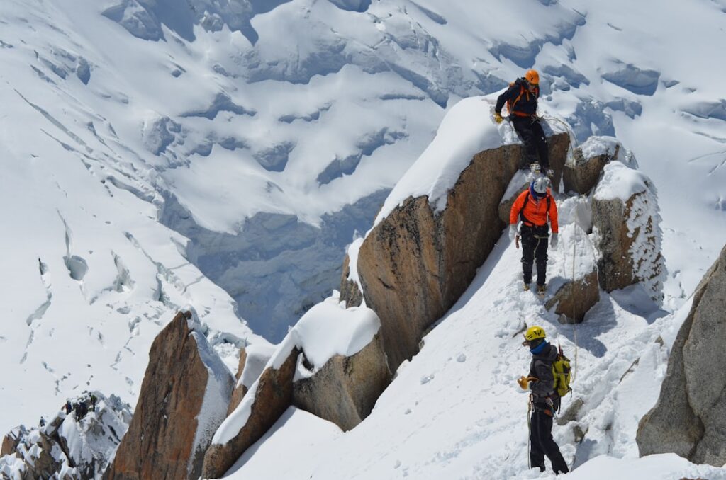 Rescue helicopter hovers above Mont Blanc's snow-covered ridge as climbers traverse the steep alpine slope under clear summer sky