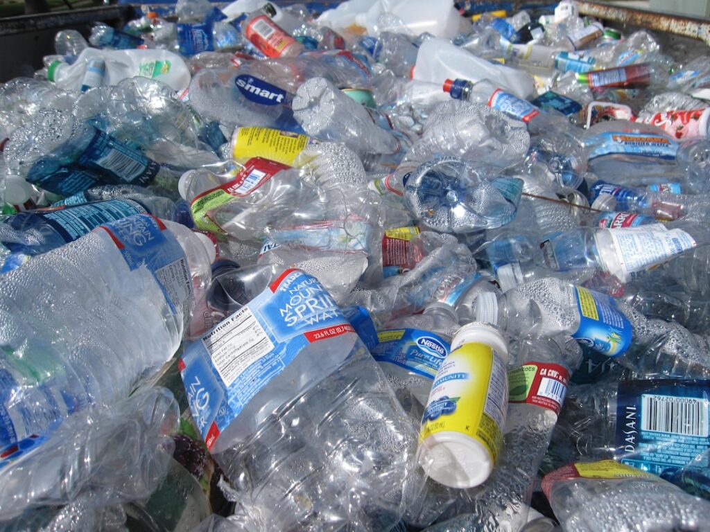 A pile of discarded plastic packaging and containers on a polluted beach near Kuala Lumpur, with waves washing debris ashore.